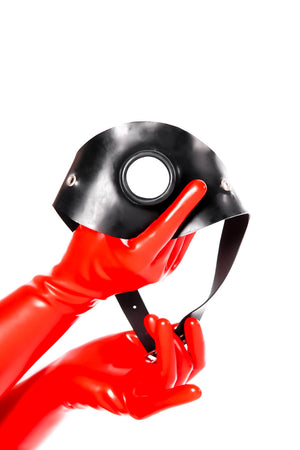 Red latex gloves holding a hollow gag on a strap.