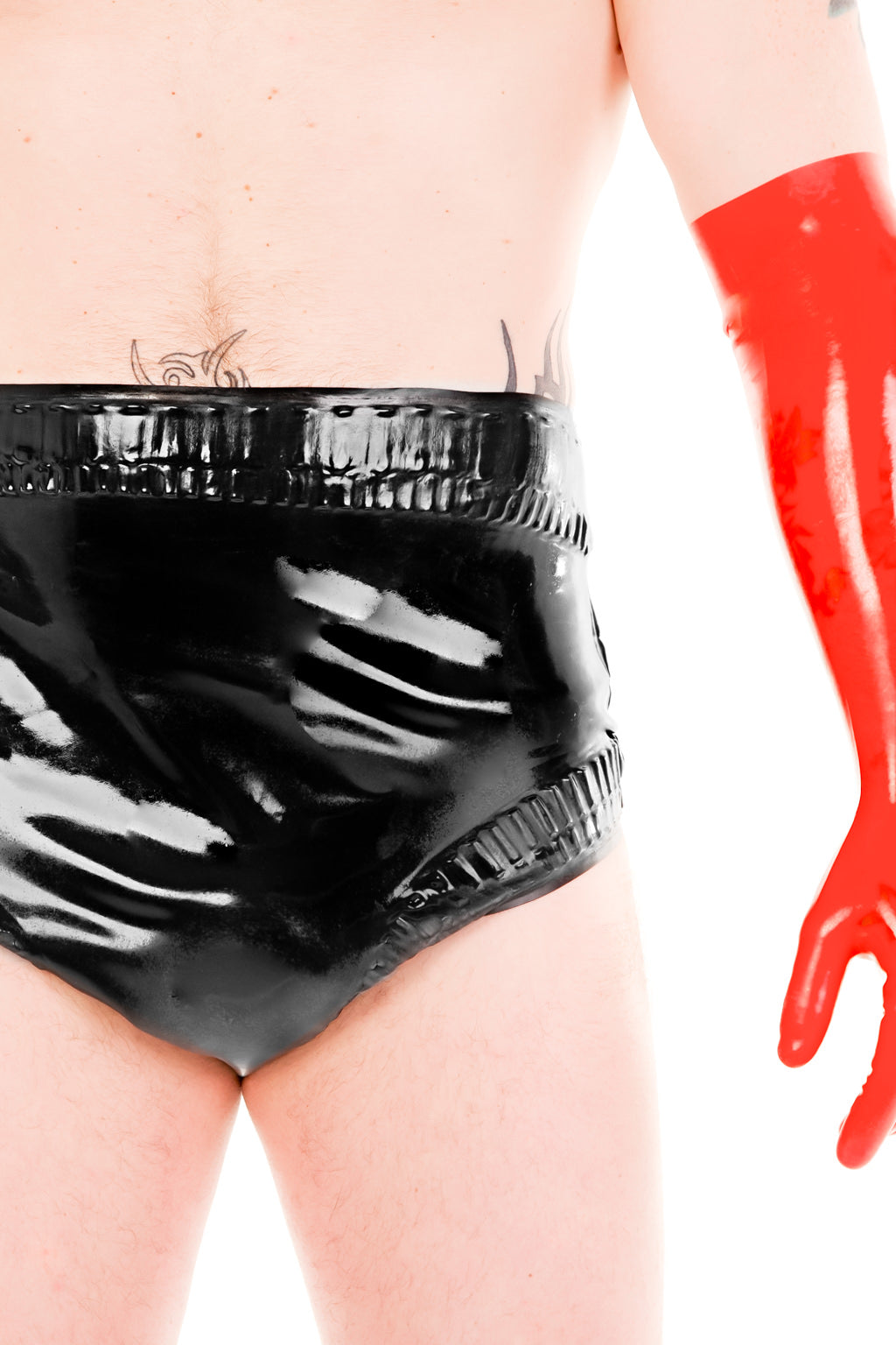A man wearing a pair of frilled latex baby pants and red elbow gloves.