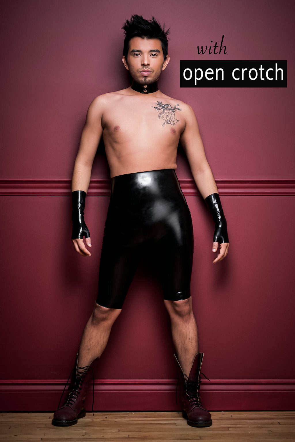 A man wearing crotchless high waisted latex bermuda shorts, black fingerless latex wrist gloves and a latex choker.