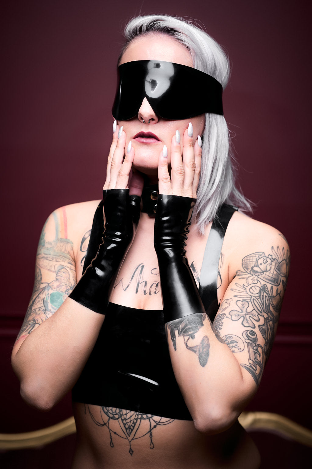 A woman wearing a latex blindfold and fingerless latex wrist gloves.