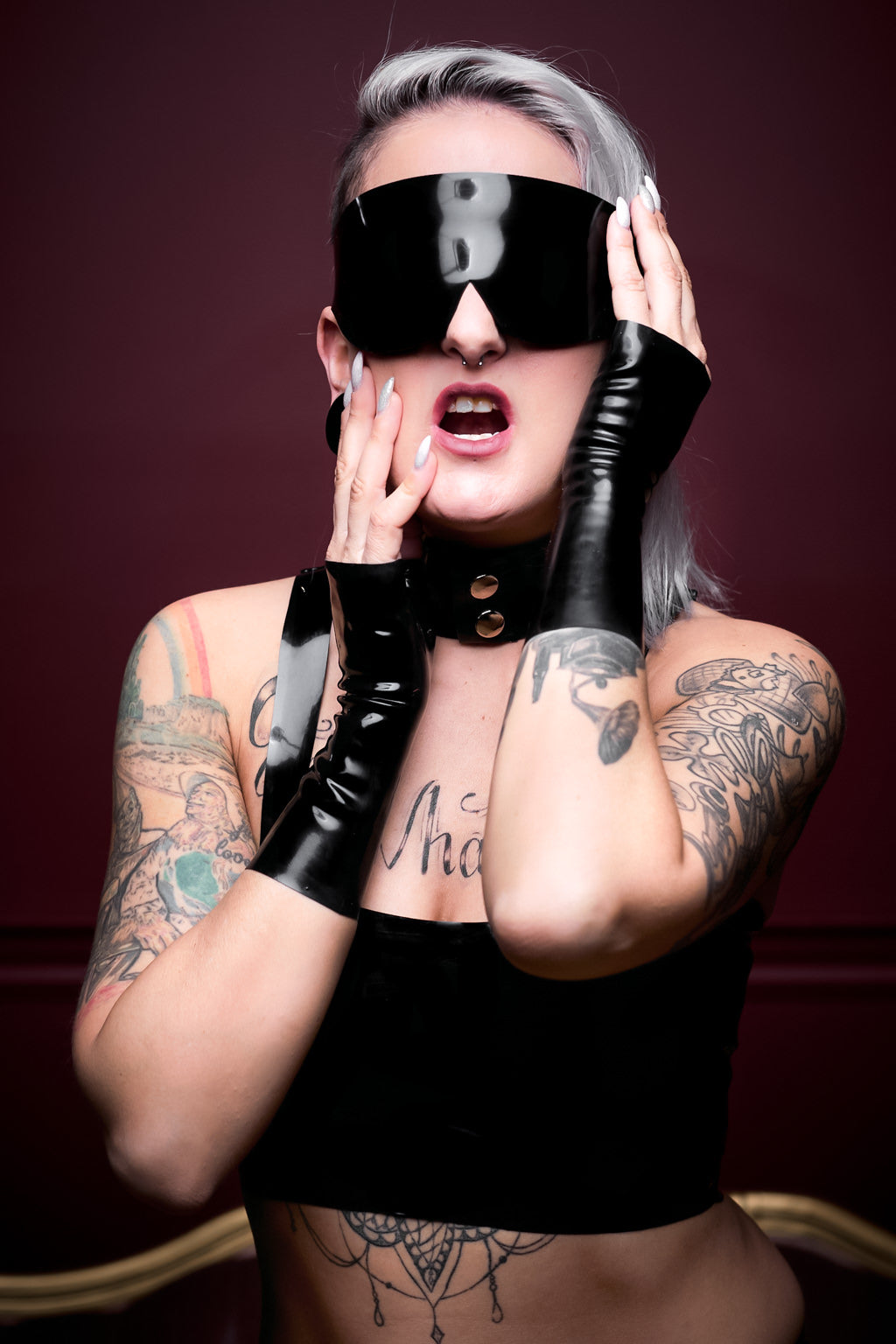 A woman wearing a latex blindfold, a latex choker and latex wrist gloves.