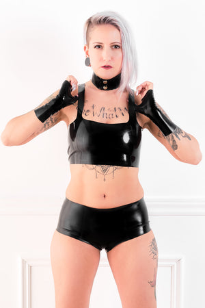 A woman wearing a latex choker, fingerless latex wrist gloves, a latex top and latex boxer shorts.