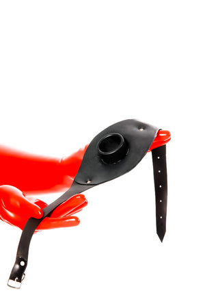 Red latex gloves holding a hollow gag on a strap.