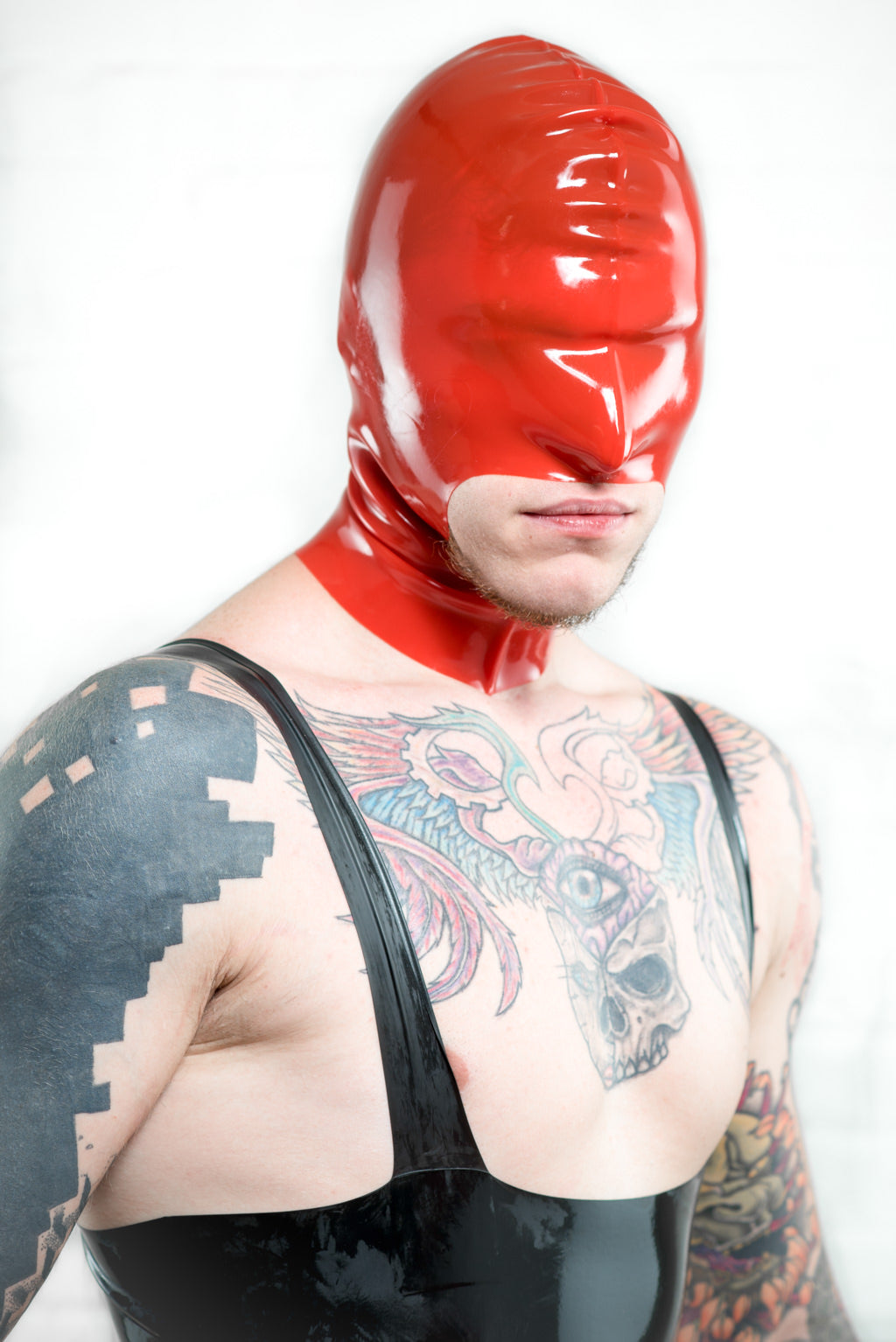 A man wearing a latex leotard and a red latex hood with large mouth.
