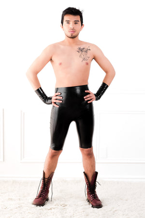 A man wearing high waisted latex bermuda shorts and latex wrist gloves.