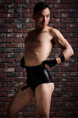 A man wearing a pair of high waisted latex underwear with a penis sheath and a latex arm band.