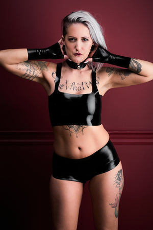 A woman wearing black latex boxer shorts with a latex camisole top and latex wrist gloves.