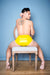 A man sitting on a chair wearing a pair of yellow latex underwear. A rear view, showing his ass.