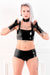 A woman wearing a black latex choker, fingerless latex wrist gloves, a latex camisole top and latex boxer shorts.
