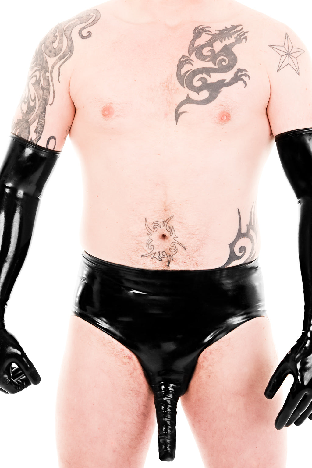 A man wearing black latex briefs with an anatomical penis sheath and latex elbow gloves.