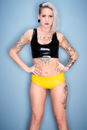 A woman wearing yellow latex panty briefs and a black latex shirt.