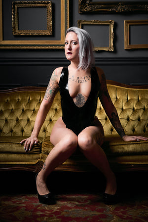 A woman sitting on a fancy couch wearing a latex leotard.